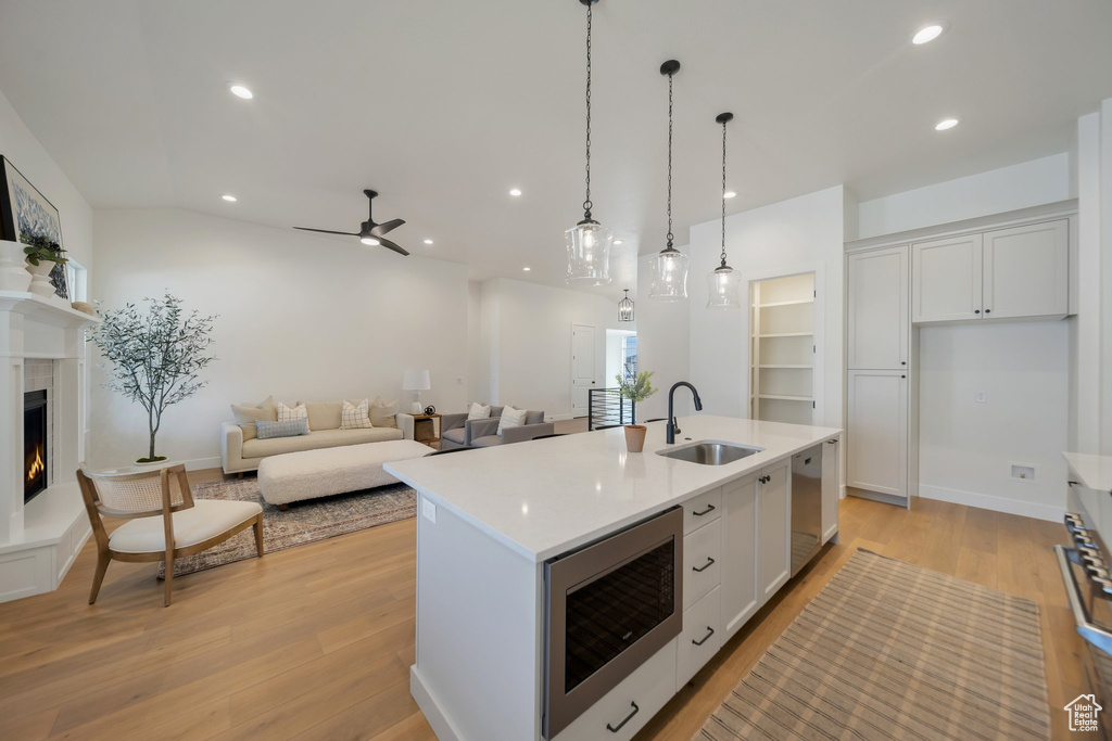 Kitchen with light hardwood / wood-style flooring, a center island with sink, sink, and white cabinetry