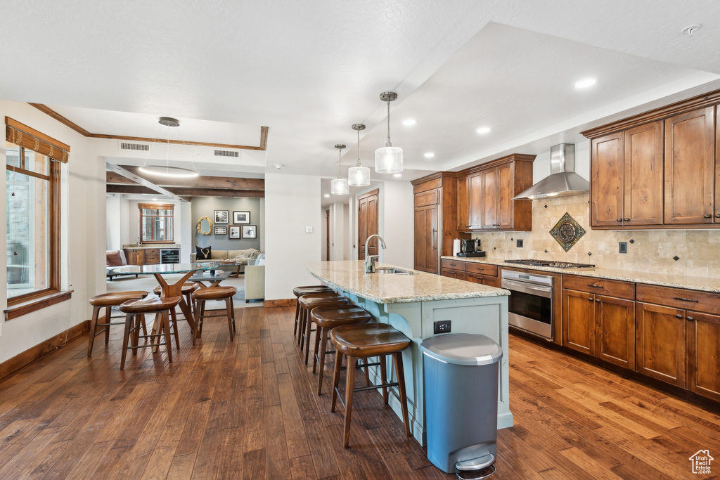 Kitchen featuring dark hardwood / wood-style floors, wall chimney exhaust hood, a kitchen island with sink, a breakfast bar, and stainless steel appliances