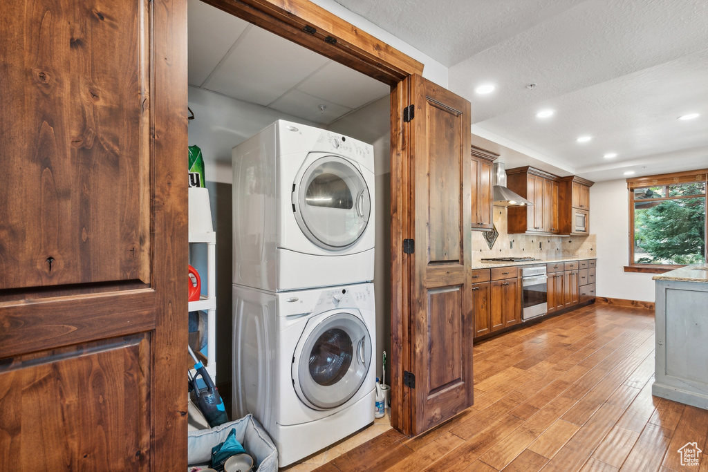 Laundry room with light hardwood / wood-style floors and stacked washing maching and dryer