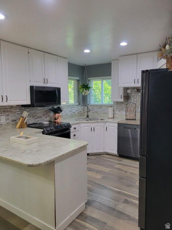 Kitchen featuring light hardwood / wood-style floors, white cabinetry, sink, black appliances, and kitchen peninsula