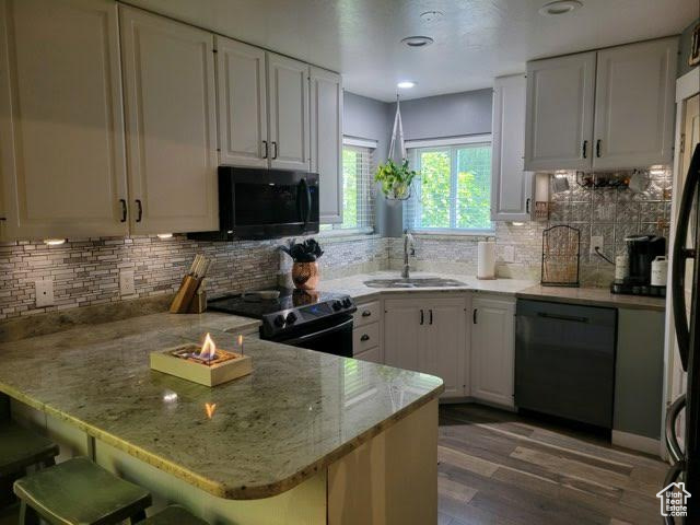 Kitchen with black appliances, wood-type flooring, kitchen peninsula, sink, and white cabinets