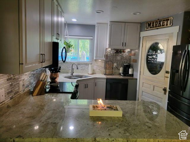 Kitchen with black appliances, light stone counters, decorative backsplash, and sink