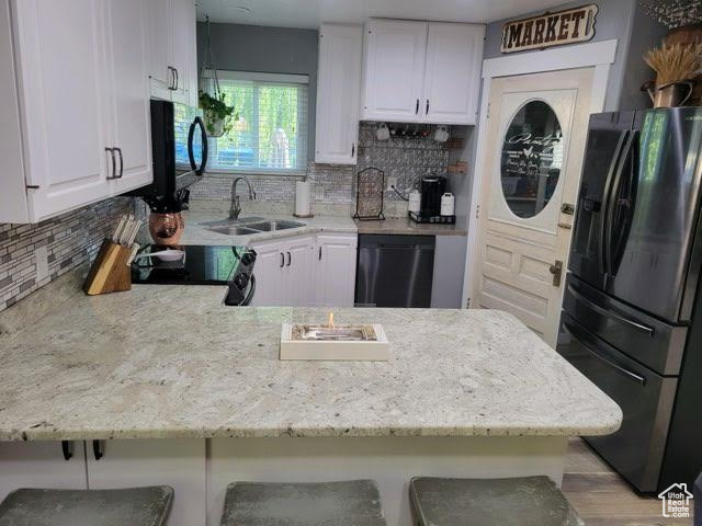 Kitchen featuring black appliances, kitchen peninsula, sink, a breakfast bar area, and white cabinets