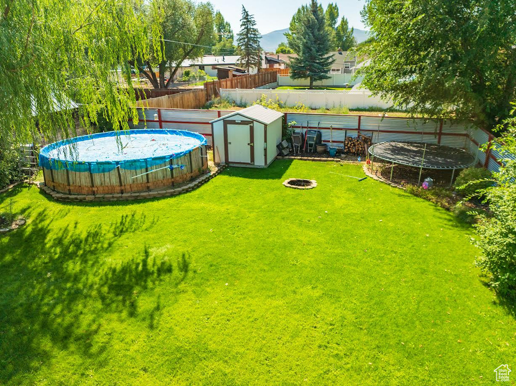 View of yard featuring a fire pit, a trampoline, and a shed