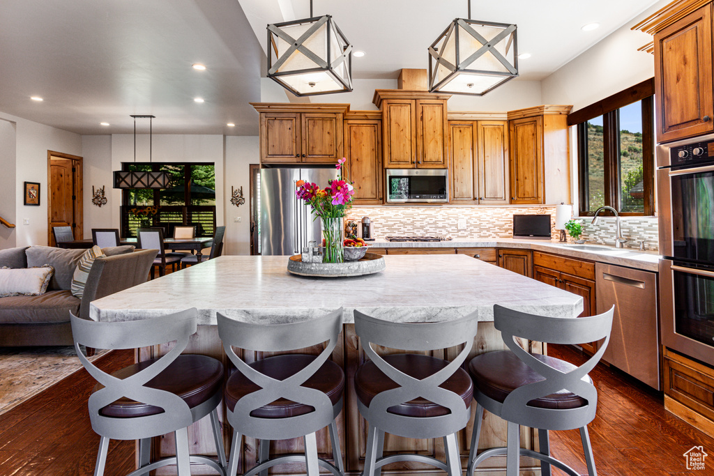 Kitchen with stainless steel appliances, sink, dark wood-type flooring, pendant lighting, and a kitchen island