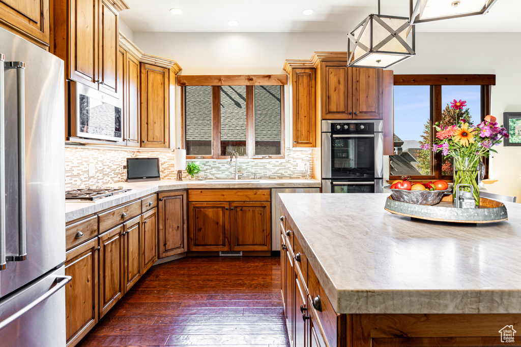 Kitchen with stainless steel appliances, sink, decorative backsplash, hanging light fixtures, and dark wood-type flooring