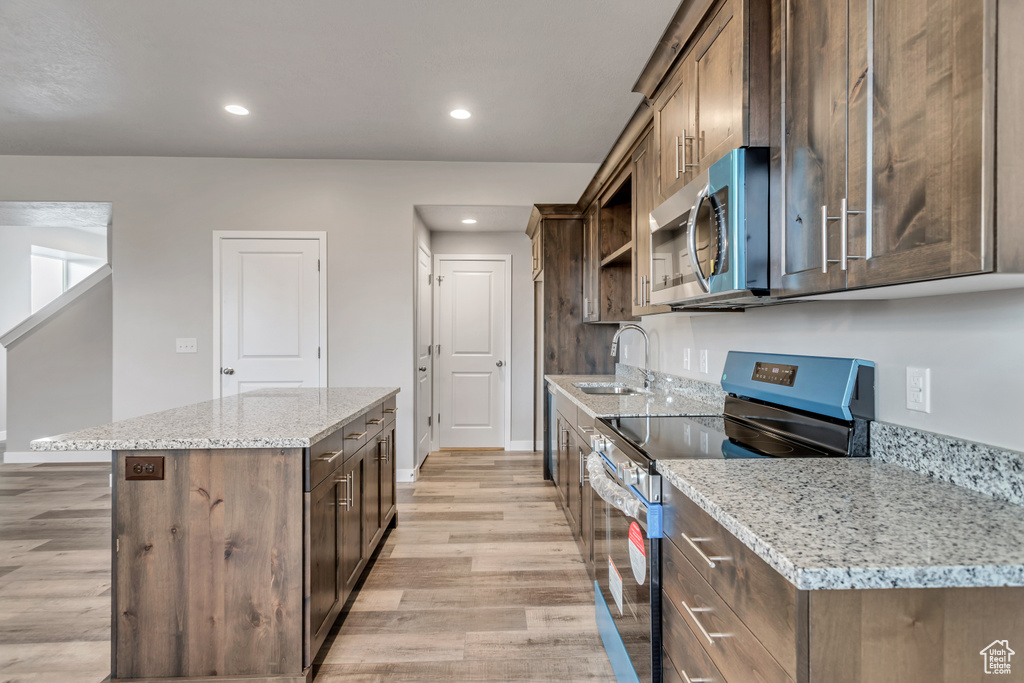 Kitchen featuring a kitchen island, light stone countertops, light hardwood / wood-style floors, stainless steel appliances, and sink