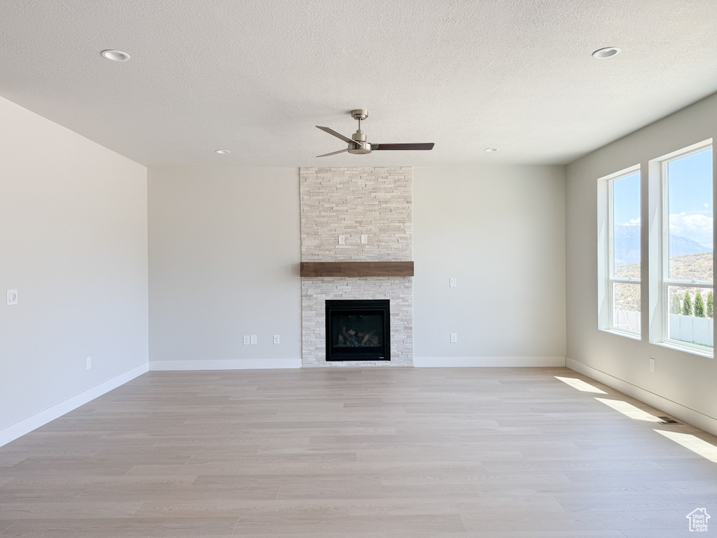 Unfurnished living room with light wood finished floors, a ceiling fan, a textured ceiling, a fireplace, and recessed lighting