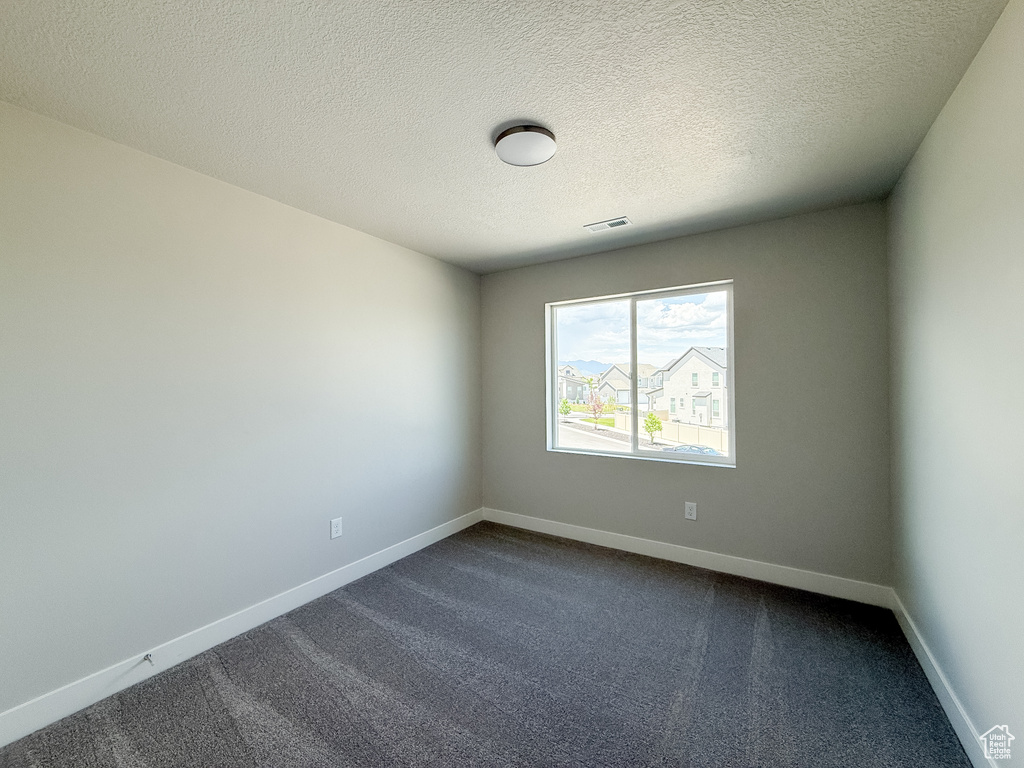 Spare room with dark colored carpet and a textured ceiling