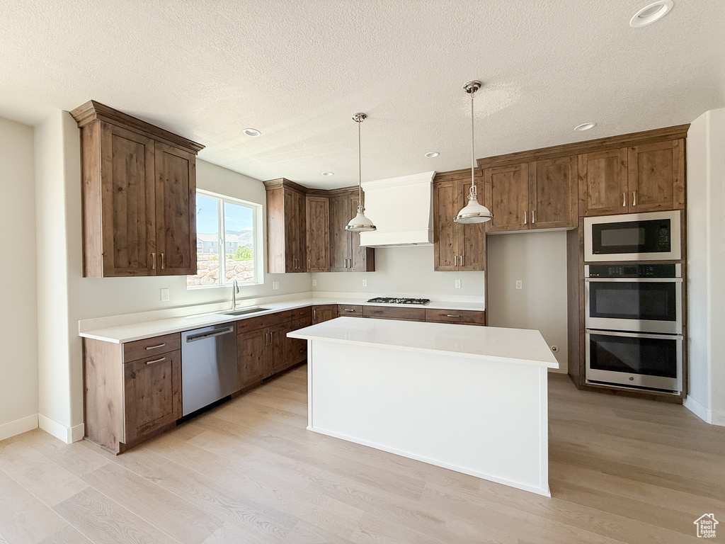 Kitchen featuring appliances with stainless steel finishes, light wood finished floors, a center island, recessed lighting, and custom range hood
