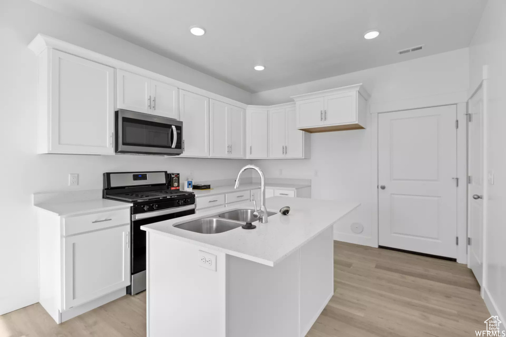 Kitchen featuring appliances with stainless steel finishes, light hardwood / wood-style floors, an island with sink, sink, and white cabinets