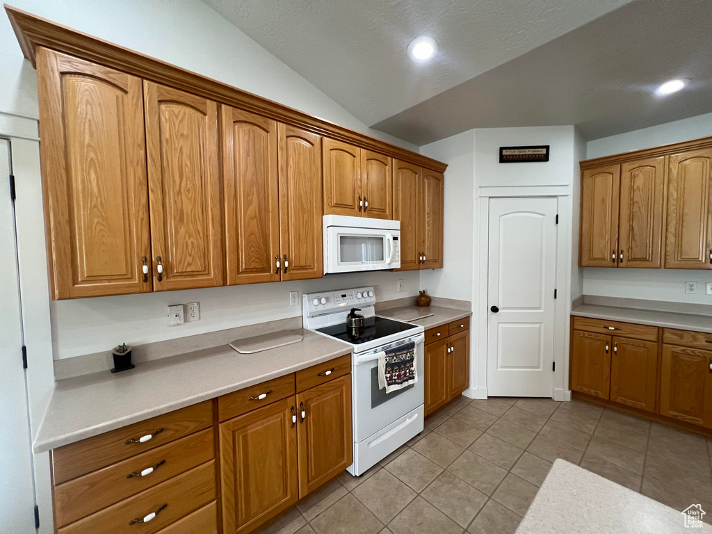 Kitchen with lofted ceiling, white appliances, and light tile patterned flooring