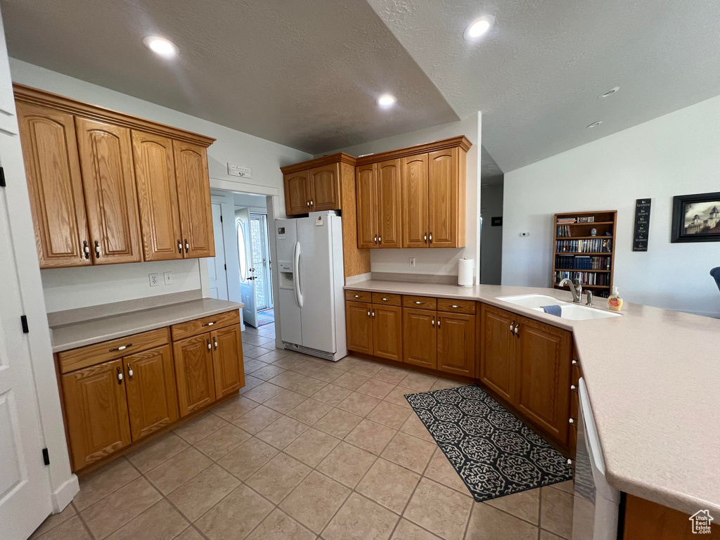 Kitchen with white refrigerator with ice dispenser, kitchen peninsula, sink, vaulted ceiling, and light tile patterned flooring