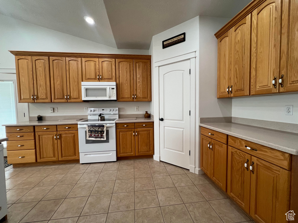 Kitchen with white appliances, light tile patterned flooring, and lofted ceiling