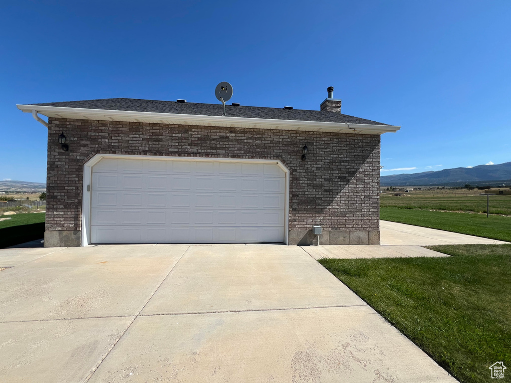 View of side of property featuring a garage, a mountain view, and a lawn