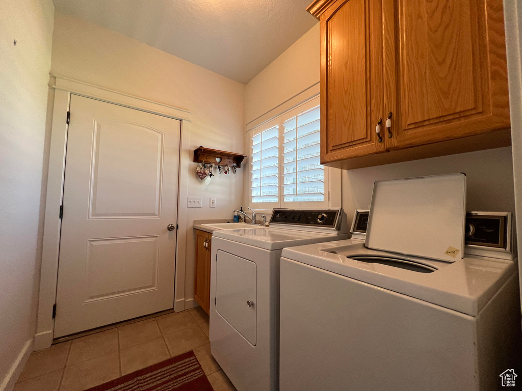 Laundry area with washing machine and clothes dryer, cabinets, sink, and light tile patterned floors