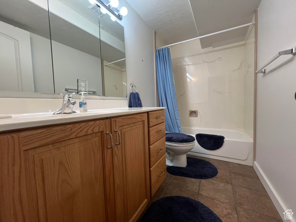 Full bathroom featuring tile patterned floors, toilet, vanity, shower / bath combo with shower curtain, and a textured ceiling