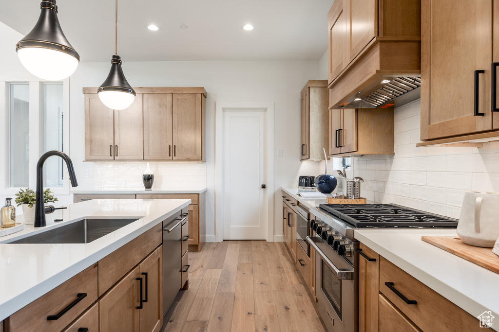 Kitchen featuring custom range hood, light hardwood / wood-style floors, stainless steel appliances, decorative light fixtures, and sink