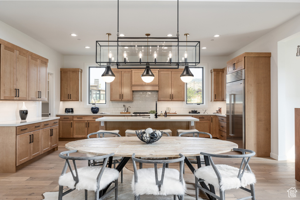 Kitchen featuring stainless steel appliances, a center island with sink, hanging light fixtures, and light wood-type flooring