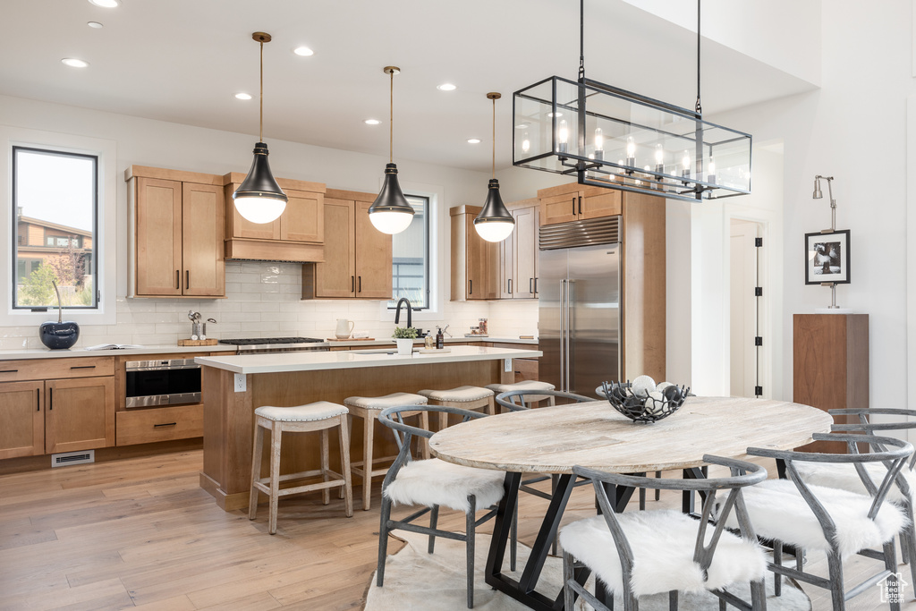 Kitchen with hanging light fixtures, a center island, light hardwood / wood-style flooring, and stainless steel appliances