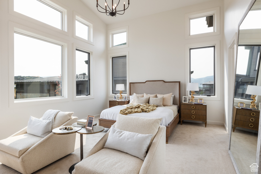 Bedroom with a high ceiling, light colored carpet, and a notable chandelier