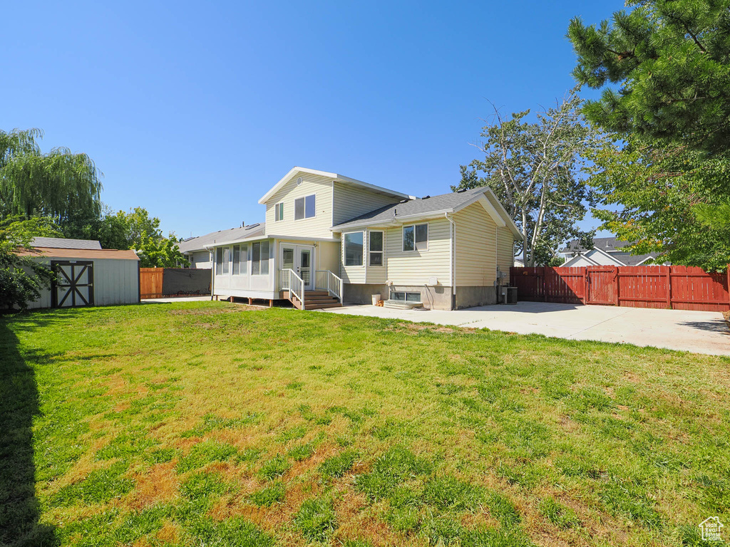 Rear view of house featuring a storage unit, a lawn, and a patio