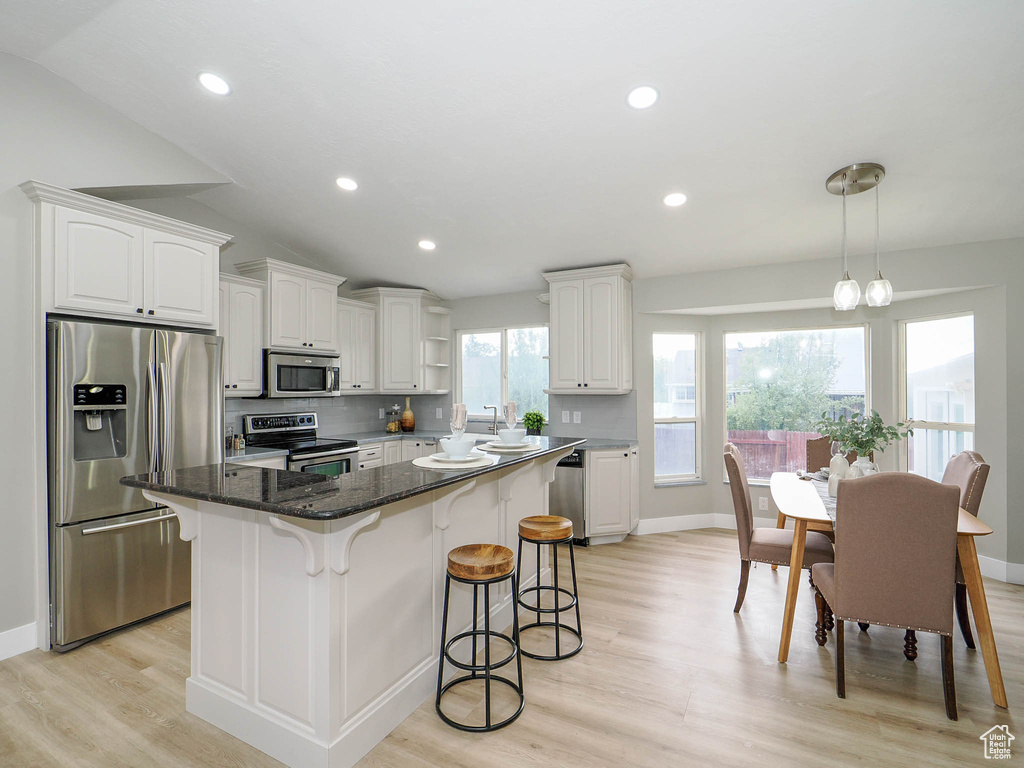 Kitchen with white cabinetry, vaulted ceiling, a center island, hanging light fixtures, and appliances with stainless steel finishes