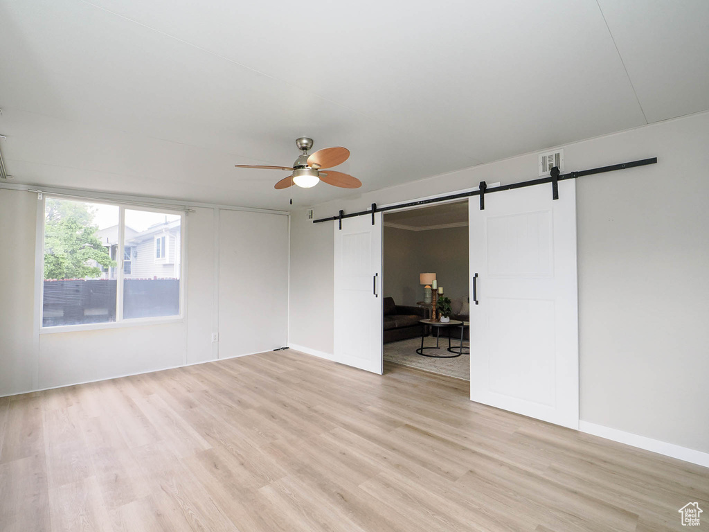 Empty room with a barn door, ceiling fan, and light wood-type flooring