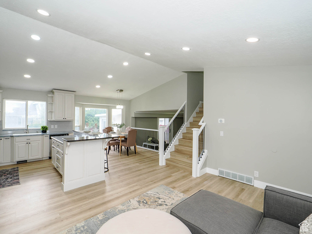 Kitchen featuring white cabinets, decorative light fixtures, light wood-type flooring, lofted ceiling, and a kitchen bar