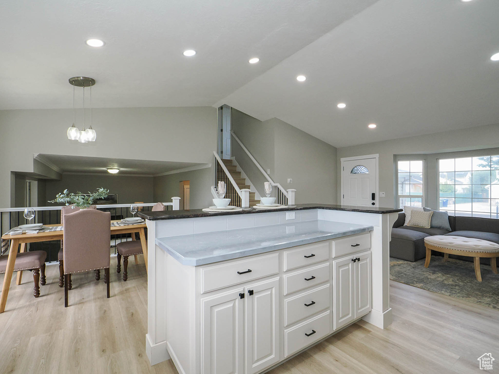 Kitchen featuring decorative light fixtures, light wood-type flooring, white cabinetry, lofted ceiling, and a center island with sink