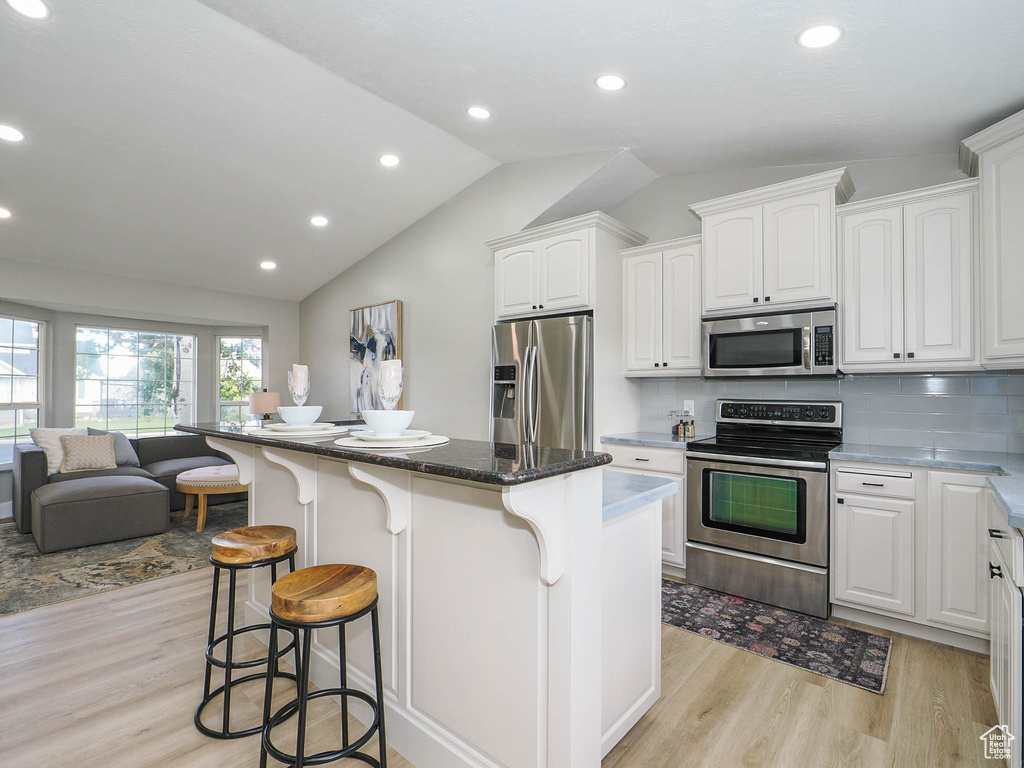 Kitchen with vaulted ceiling, a kitchen island, appliances with stainless steel finishes, white cabinets, and light hardwood / wood-style floors