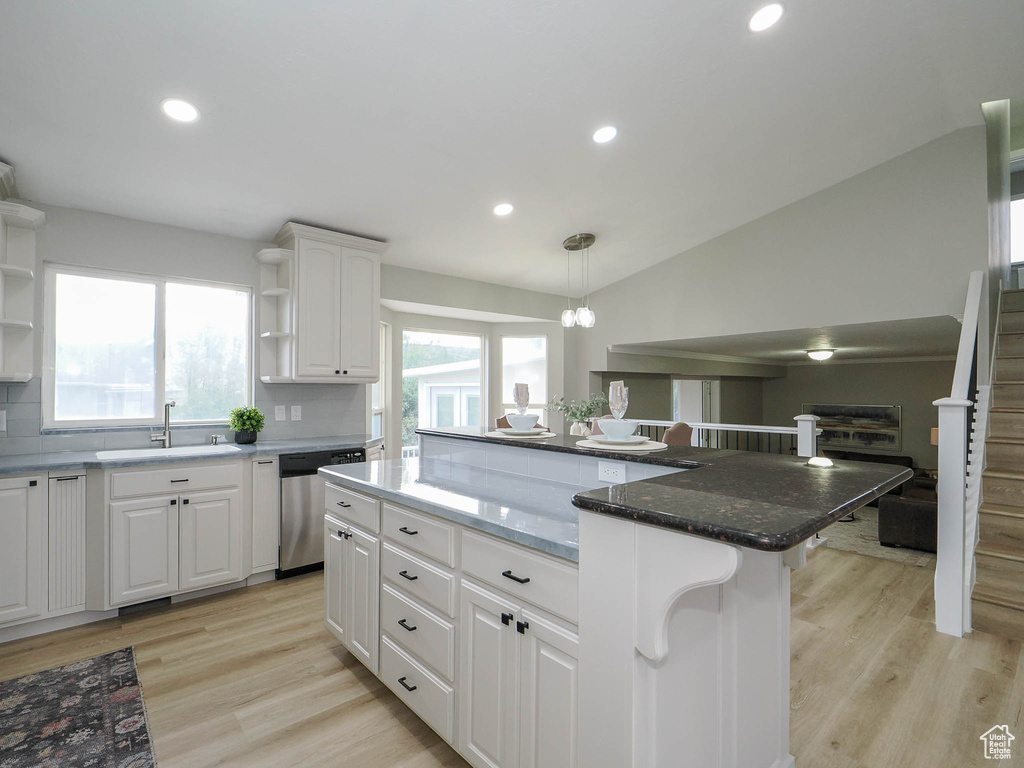 Kitchen with white cabinets, hanging light fixtures, dishwasher, a center island, and lofted ceiling