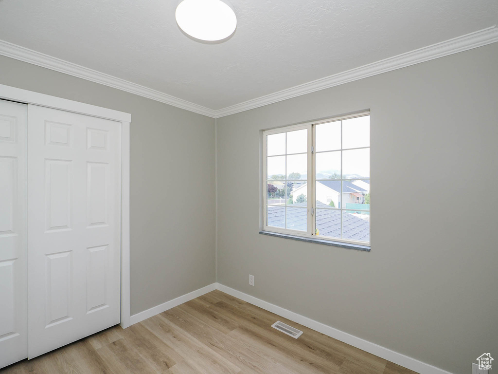 Unfurnished bedroom featuring ornamental molding, a closet, and light wood-type flooring