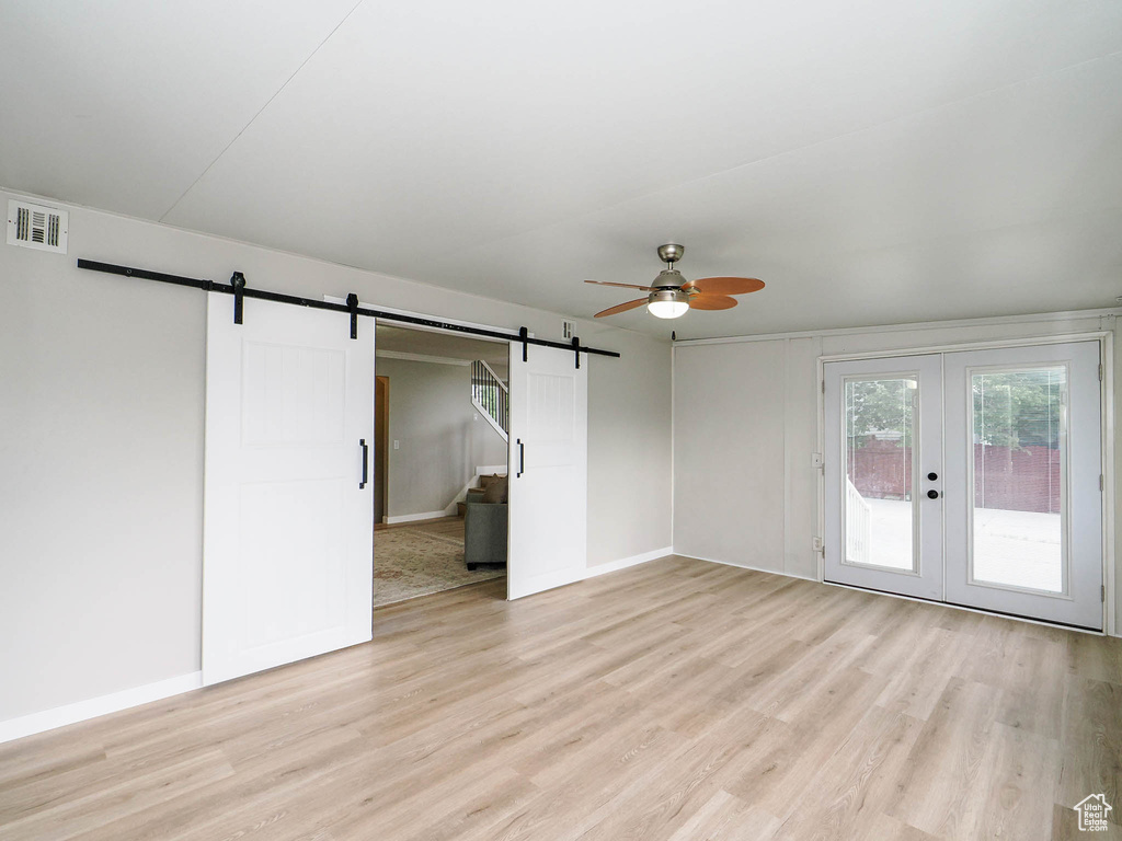 Unfurnished room featuring a barn door, ceiling fan, and light hardwood / wood-style floors