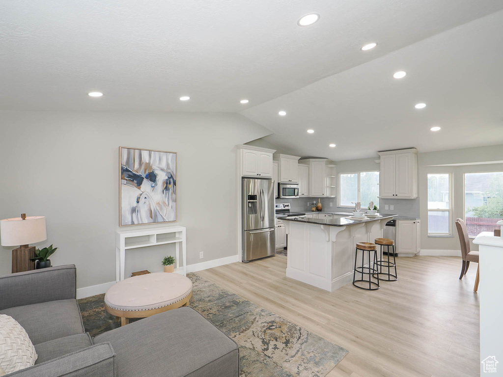 Kitchen featuring appliances with stainless steel finishes, a kitchen bar, a center island, lofted ceiling, and white cabinets