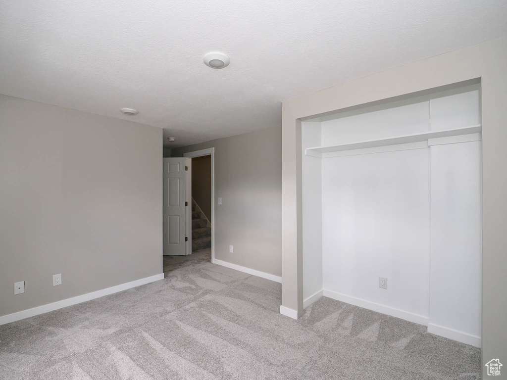 Unfurnished bedroom featuring a textured ceiling, light colored carpet, and a closet