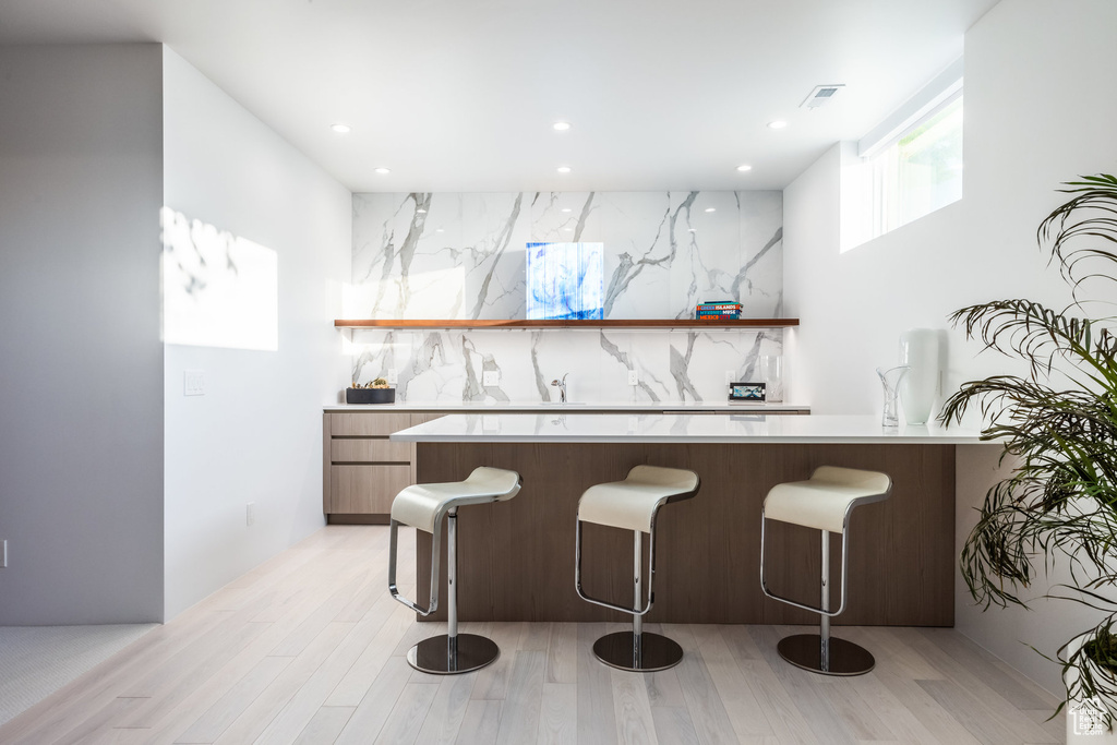 Bar featuring backsplash and light wood-type flooring