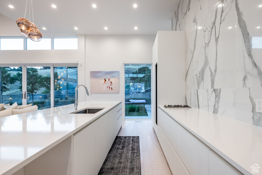 Kitchen featuring pendant lighting, white cabinetry, sink, and light hardwood / wood-style floors