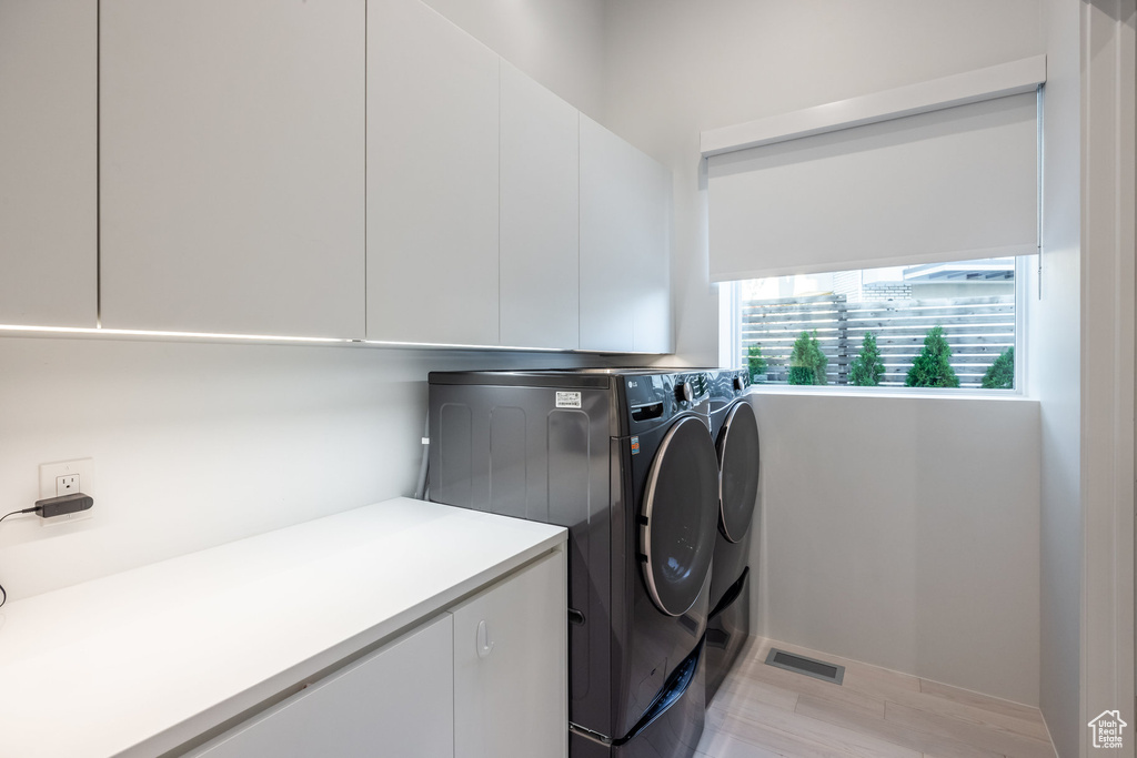 Laundry area with light wood-type flooring, cabinets, and separate washer and dryer