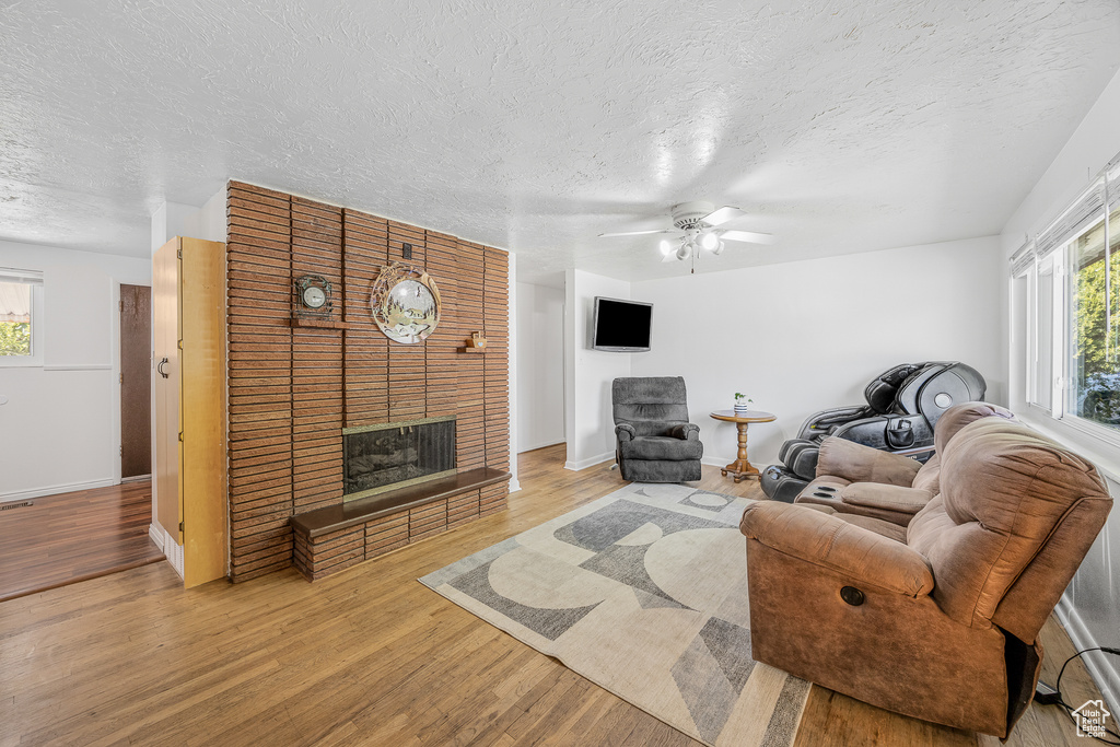 Living room with a textured ceiling, light hardwood / wood-style flooring, ceiling fan, and a fireplace