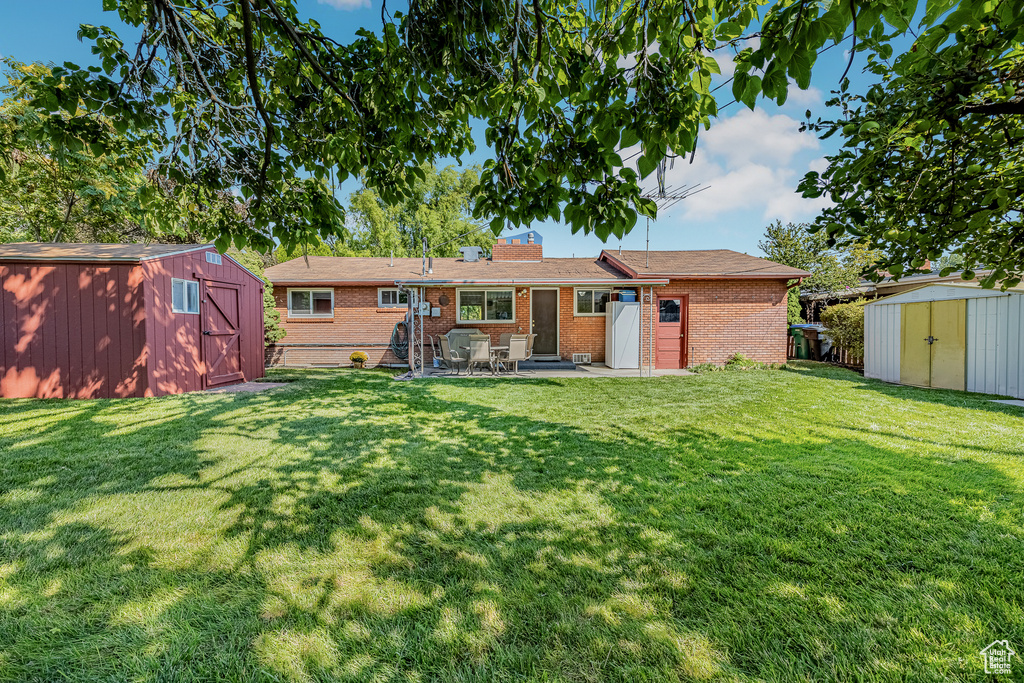 Rear view of property featuring a lawn, a patio, and a shed