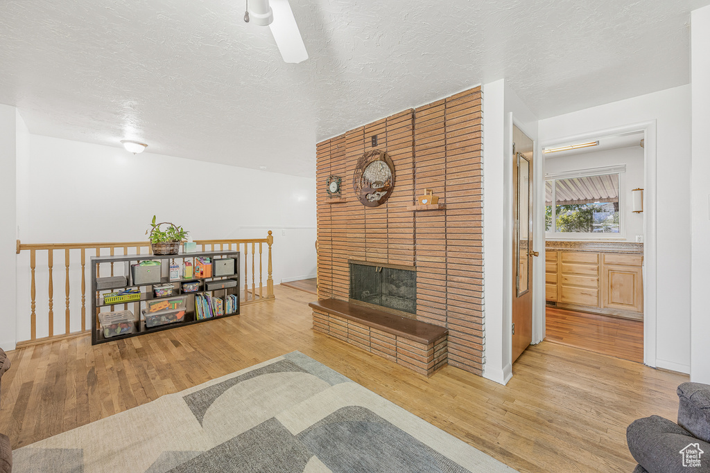 Living room with a textured ceiling, ceiling fan, light wood-type flooring, and a brick fireplace