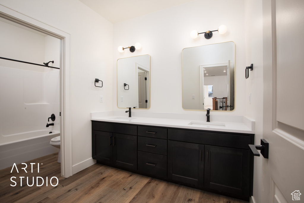 Full bathroom featuring vanity, toilet, wood-type flooring, and washtub / shower combination