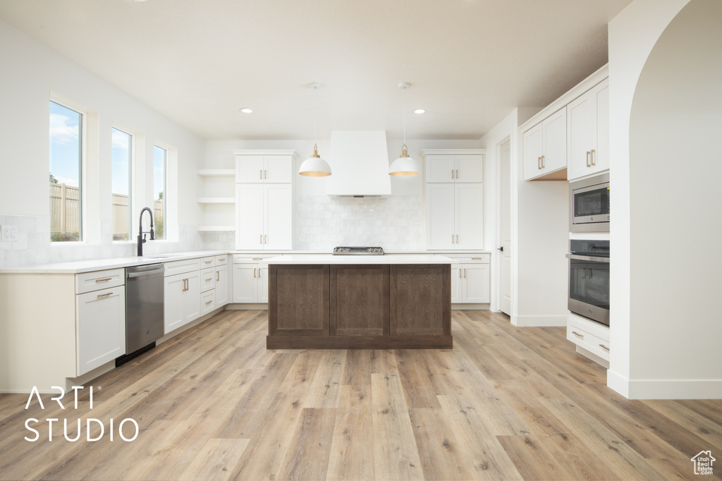 Kitchen with white cabinets, a center island, light wood-type flooring, appliances with stainless steel finishes, and decorative backsplash