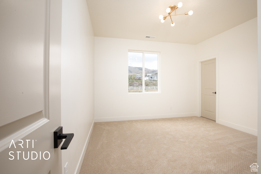 Spare room with light colored carpet and a chandelier