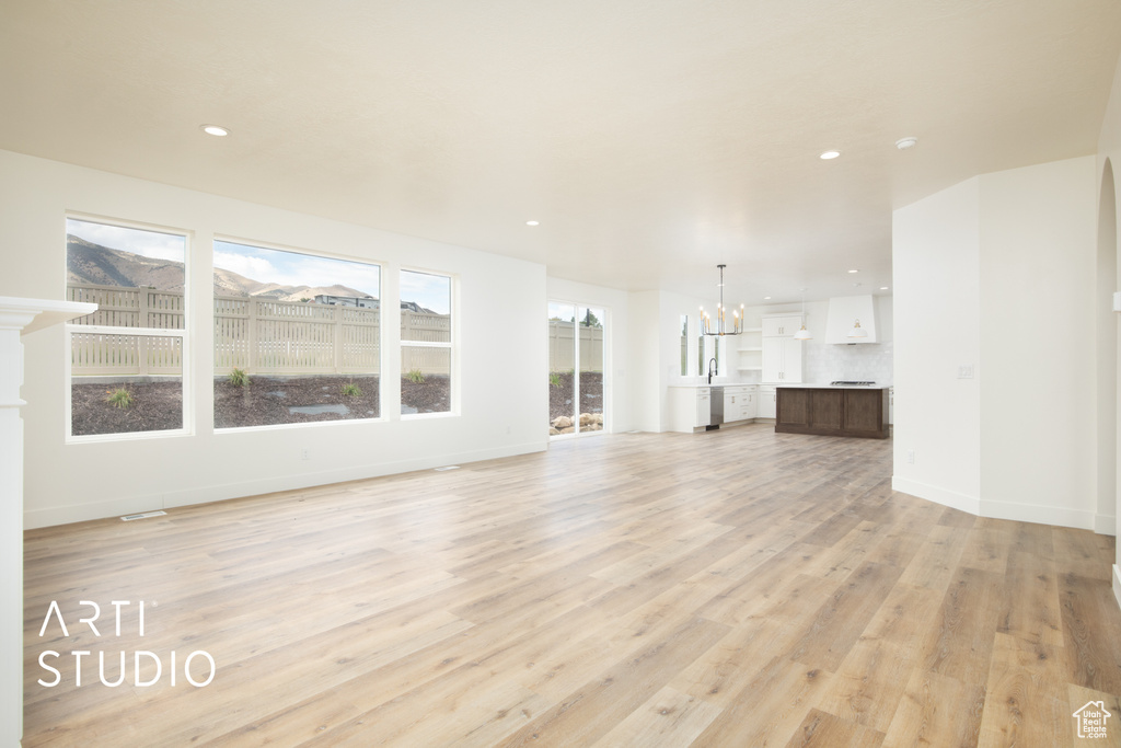 Unfurnished living room with sink, a chandelier, and light hardwood / wood-style floors