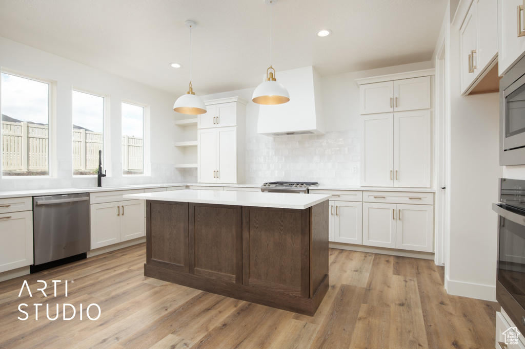 Kitchen featuring light hardwood / wood-style flooring, appliances with stainless steel finishes, white cabinetry, pendant lighting, and a kitchen island