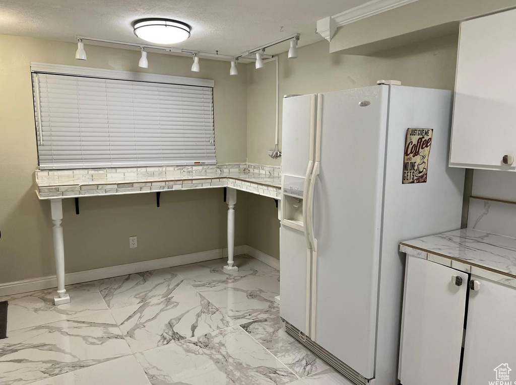 Kitchen with track lighting, white fridge with ice dispenser, white cabinetry, and a textured ceiling