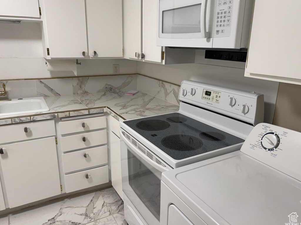 Kitchen with white appliances, tasteful backsplash, washer / dryer, sink, and white cabinetry