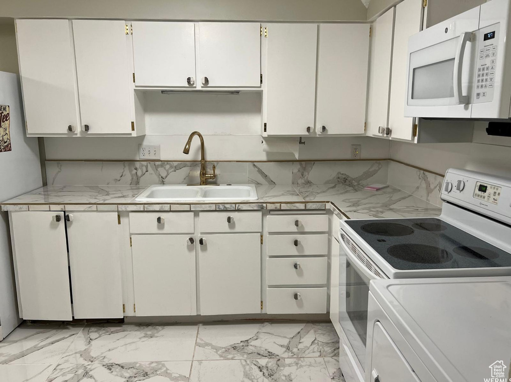 Kitchen featuring sink, white appliances, white cabinets, and tasteful backsplash